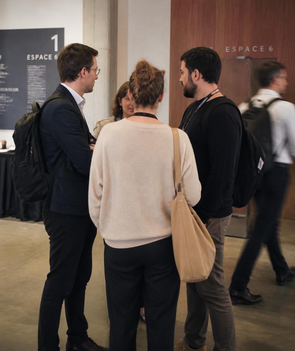 A small huddle of people in conversation in a conference corridor, seen from behind